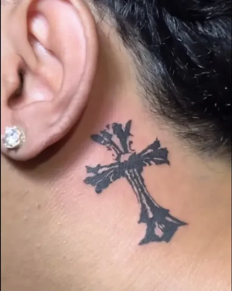Small blackwork cross tattoo behind the ear on the neck